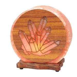 K&ouml;nnte beinhalten: Eine runde Himalaya-Salzlampe mit einem Holzsockel und einem geschnitzten Kristallmuster. Die Lampe ist eingeschaltet und leuchtet orange.