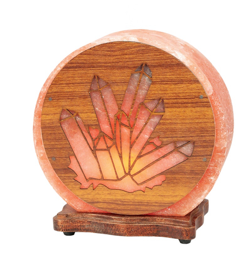 K&ouml;nnte beinhalten: Eine runde Himalaya-Salzlampe mit einem Holzsockel und einem geschnitzten Kristallmuster. Die Lampe ist eingeschaltet und leuchtet orange.