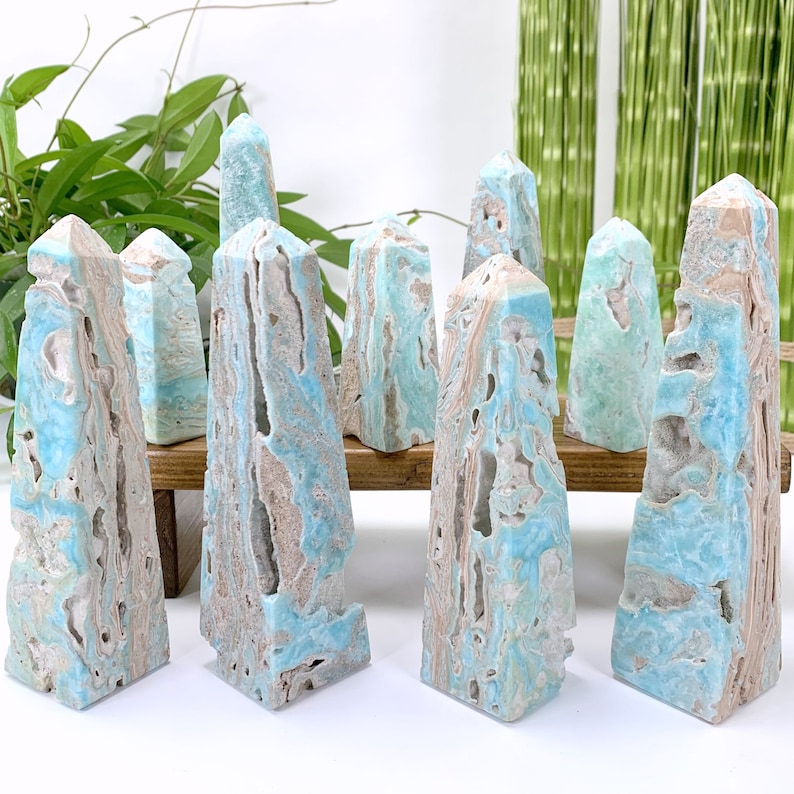 May include: A collection of eight blue and white calcite crystal points, also known as angel wing calcite, arranged on a wooden stand. The crystals have a unique, layered, and striated appearance.
