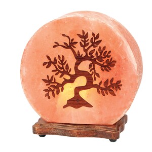 K&ouml;nnte beinhalten: Eine runde Himalaya-Salzlampe mit einem geschnitzten Baumdesign. Die Lampe ist beleuchtet und leuchtet orange. Sie steht auf einem Holzsockel.