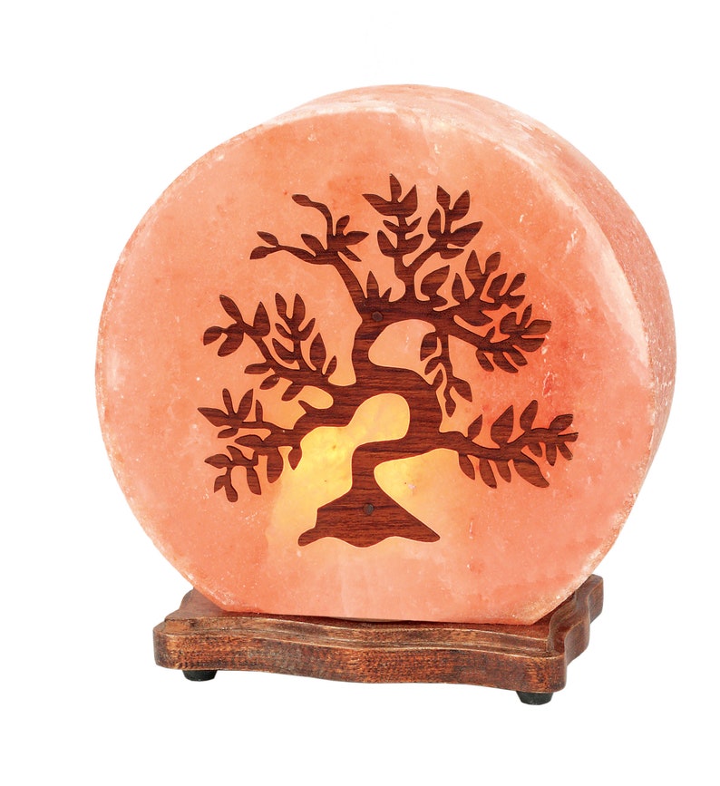 K&ouml;nnte beinhalten: Eine runde Himalaya-Salzlampe mit einem geschnitzten Baumdesign. Die Lampe ist beleuchtet und leuchtet orange. Sie steht auf einem Holzsockel.