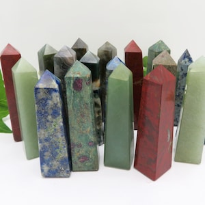 May include: A collection of 18 polished gemstone points in various colours, including green, red, blue, and grey. The points are arranged in a semi-circle on a white surface.