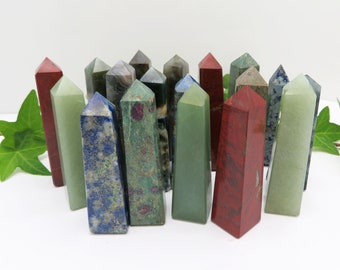 May include: A collection of 18 polished gemstone points in various colors, including green, red, blue, and gray. The points are arranged in a semi-circle on a white surface.