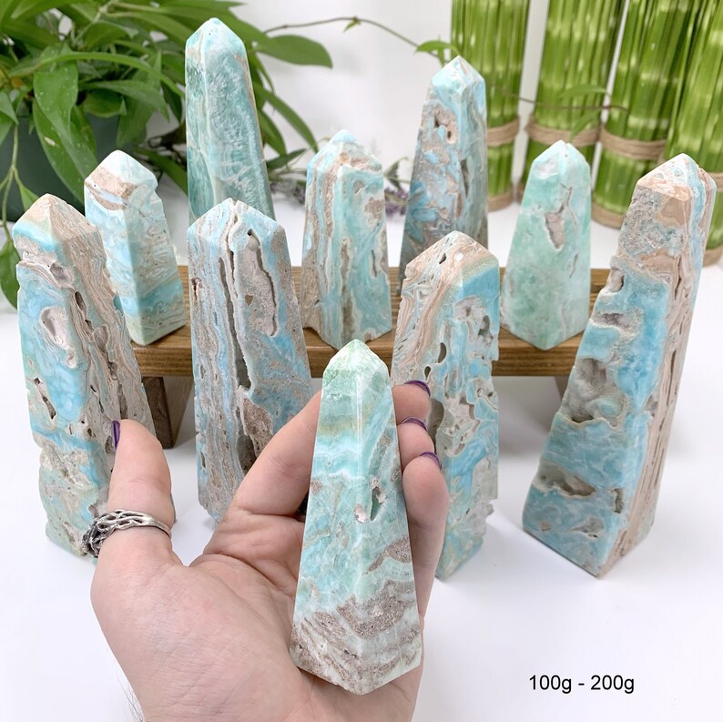 May include: A group of 10 blue and brown aragonite crystal points, some are in a hand, others are on a wooden stand. The points are 100g to 200g each.