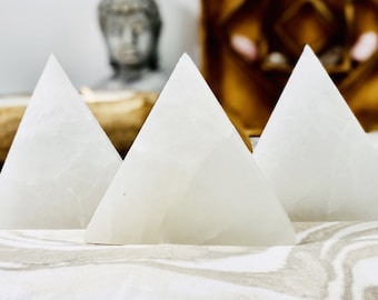 Puede incluir: Tres pirámides de cristal de selenita blanca dispuestas en fila sobre una superficie con estampado blanco y marrón.
