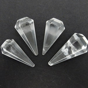 Może przedstawiać: Cztery przezroczyste kryształowe punkty kwarcu, każdy z fasetowaną, spiczastą końcówką. Kryształy są ułożone w półkole na czarnym tle.