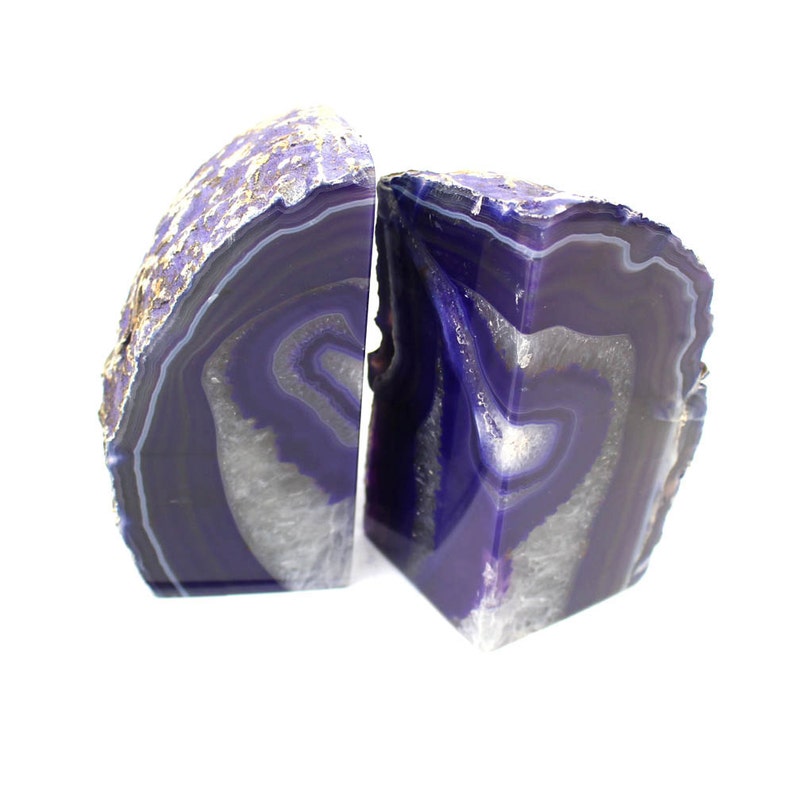 May include: A pair of purple agate bookends with white and gray banding. The bookends are made from natural agate and have a unique, organic shape.