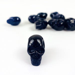 May Include: A collection of Skull Bead-- Purple Goldstone Skull Beads on white surface for reference.