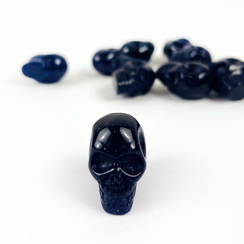 May Include: A collection of Skull Bead-- Purple Goldstone Skull Beads on white surface for reference.