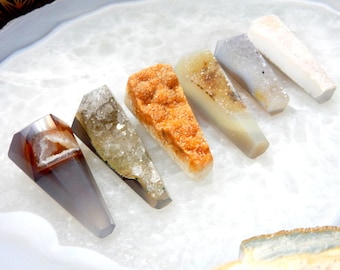 May include: Six different colored agate crystal points, each with a unique pattern and texture, arranged on a white surface.