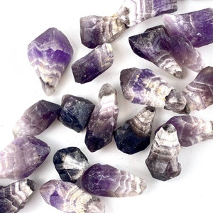 May include: A collection of amethyst crystal points with purple and white banding. The crystals are raw and have a natural, rough texture.