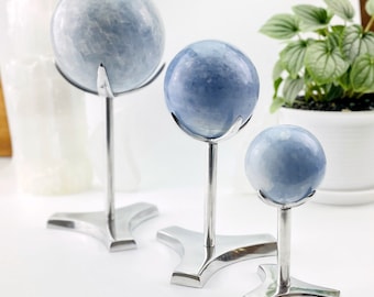 Puede incluir: Tres esferas de celestita azules de diferentes tamaños en soportes de metal plateado. Las esferas son lisas y pulidas, de color azul claro.