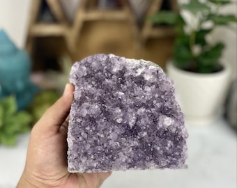 May include: A large amethyst crystal cluster with a purple hue. The crystal is raw and has a natural, rough texture. It is a beautiful example of a natural amethyst.