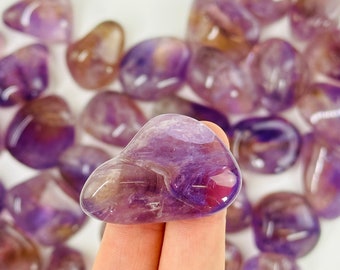 May include: A collection of amethyst tumbled stones in various shades of purple. The stones are smooth and polished, with a natural, organic shape.