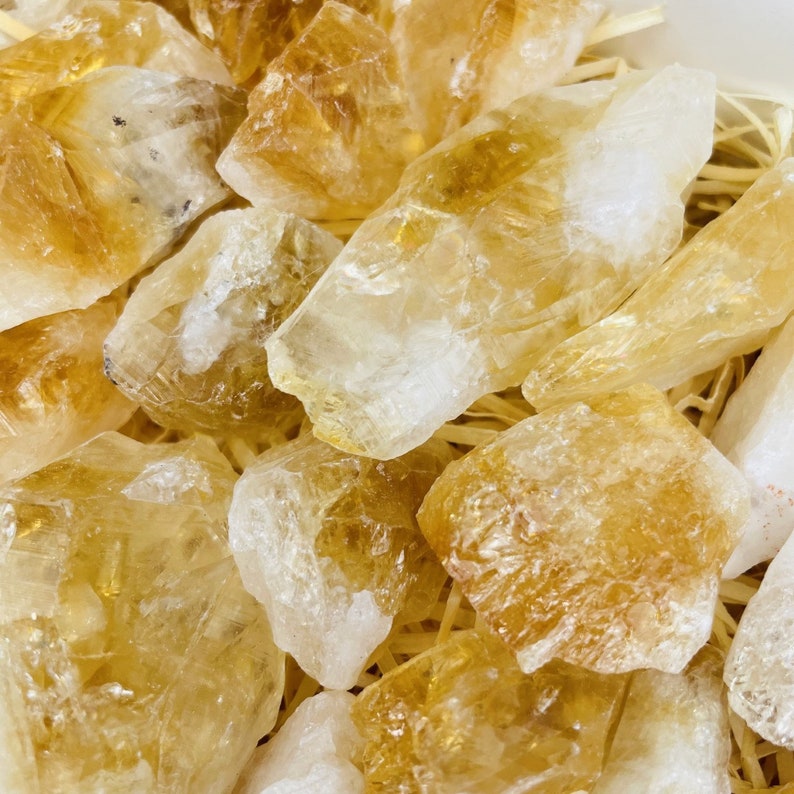 Puede incluir: Una colecci&oacute;n de cristales de citrino en bruto y naturales de varios tama&ntilde;os y formas. Los cristales son de color amarillo claro a medio y tienen una apariencia transl&uacute;cida.