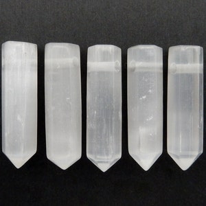 May include: Five white selenite wands with a pointed tip and a hole drilled through the top. The wands are smooth and polished.