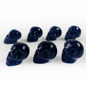 May Include: A collection of Skull Bead-- Purple Goldstone Skull Beads on white surface for reference.