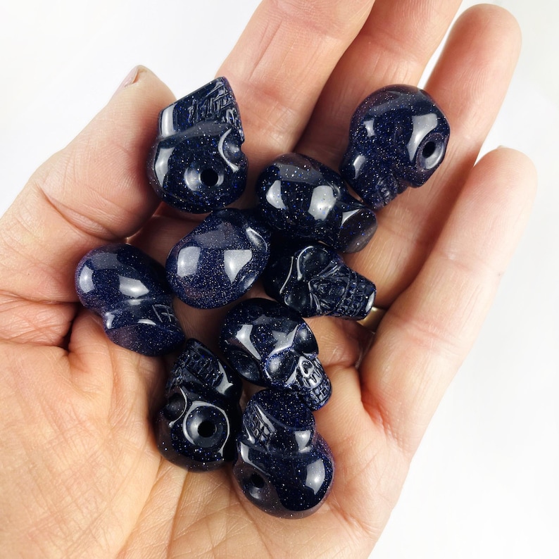 May Include: A collection of Skull Bead-- Purple Goldstone Skull Beads on palm of hand for reference.