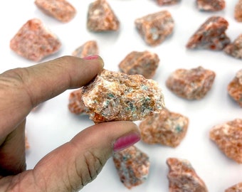 May include: A collection of orange and white rough carnelian crystals. The crystals are various sizes and shapes, with some having a green tint.