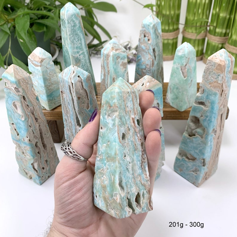 May include: A collection of 10 blue and brown aragonite crystal points, also known as blue calcite, arranged on a wooden stand. The points are approximately 201g to 300g each.