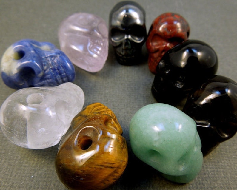 Puede incluir: Una colecci&oacute;n de diez peque&ntilde;as cuentas de cristal en forma de calavera en varios colores, incluyendo transparente, rosa, azul, verde, marr&oacute;n, negro y rojo.