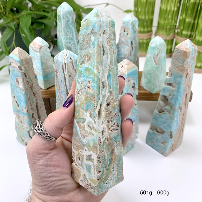 May include: A collection of blue and green celestite crystal points, some with white and brown inclusions, arranged on a wooden surface. The points are polished and have a smooth, glassy finish. The text "501g - 6000g" is visible at the bottom of the image.