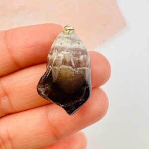 May include: A dark grey and white crystal pendant with a gold bail. The crystal is a natural, rough-cut shape.