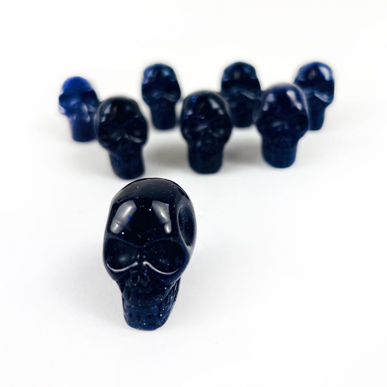 May Include: A collection of Skull Bead-- Purple Goldstone Skull Beads on white surface for reference.