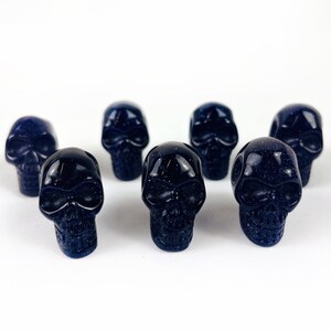May Include: A collection of Skull Bead-- Purple Goldstone Skull Beads on white surface for reference.