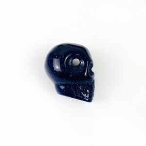 May Include: Skull Bead-- Purple Goldstone Skull Bead on white surface for reference.