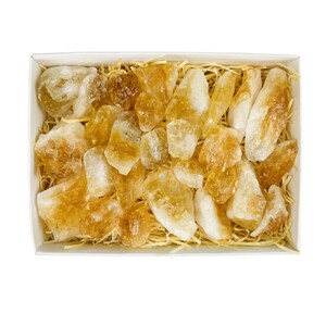 Puede incluir: Una caja llena de cristales de citrino dorado en bruto y natural. Los cristales son de varios tama&ntilde;os y formas, y est&aacute;n anidados en un lecho de material similar a la paja.