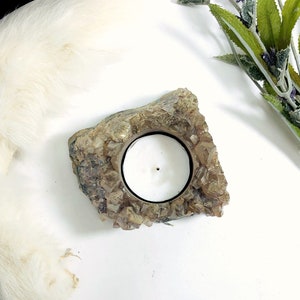May include: A brown crystal candle holder with a round opening for a tea light. The holder is made of natural quartz crystals.
