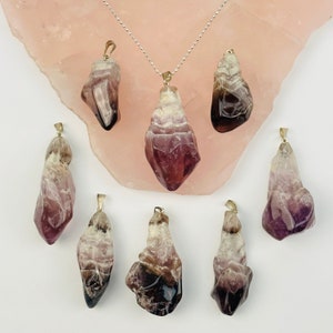 May include: Eight amethyst crystal pendants with gold bail settings. The crystals are a mix of purple, white, and brown.
