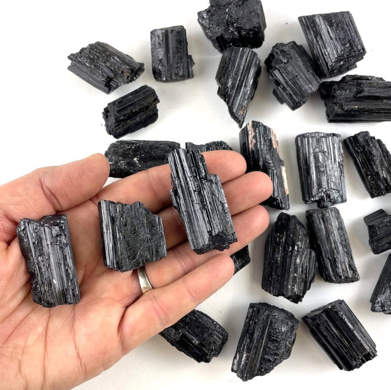 May include: A collection of black tourmaline crystals, also known as schorl, in various sizes and shapes. The crystals have a striated, black, and opaque appearance.