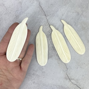 May include: Four white carved bone feathers. The feathers are detailed with carved lines and have a smooth, polished finish.