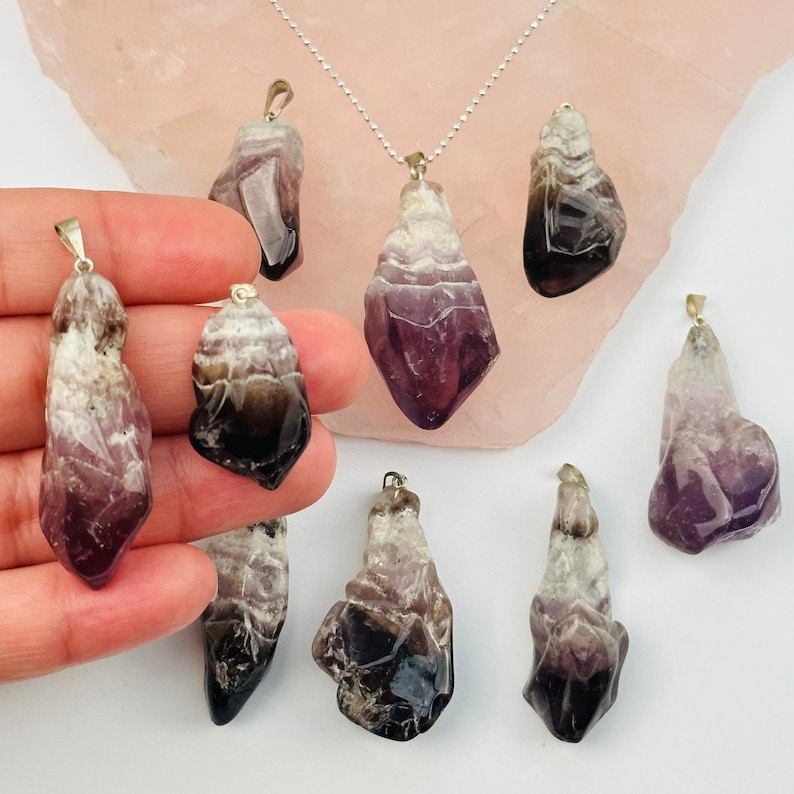 May include: Eight amethyst crystal pendants with silver bail settings. The crystals are a mix of purple and black with white banding.
