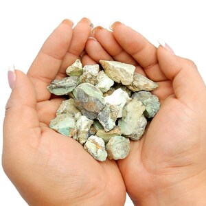 May include: A handful of green and brown stones, likely turquoise, are held in the palm of a person's hand.
