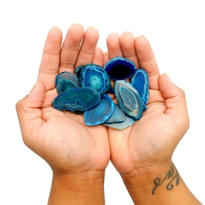 May include: A collection of blue agate slices, with varying shades of blue and white, are held in the palm of a person's hand.