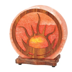 K&ouml;nnte beinhalten: Eine runde Himalaya-Salzlampe mit einem Holzrahmen, der ein geschnitztes Sonnenmotiv zeigt. Die Lampe ist eingeschaltet und leuchtet orange.