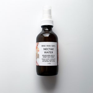 May include: A brown glass bottle with a white spray nozzle. The label reads "NECTAR WATER" and "NOURISHING ROSE & HONEY FACE TONER". The bottle contains 3 oz of product. The label also lists ingredients like Manuka Honey, Rosewater, and Red Clover.