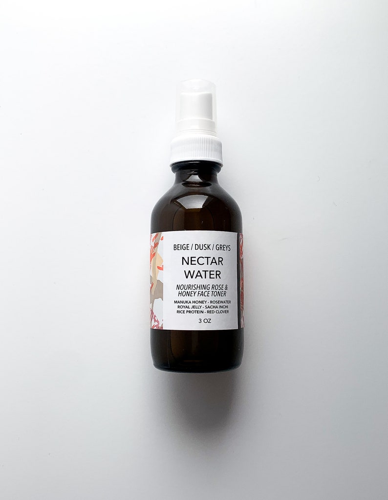 May include: A brown glass bottle with a white spray nozzle. The label reads "NECTAR WATER" and "NOURISHING ROSE & HONEY FACE TONER". The bottle contains 3 oz of product. The label also lists ingredients like Manuka Honey, Rosewater, and Red Clover.