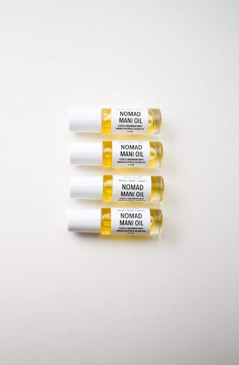 Puede incluir: Cuatro botellas de vidrio transparente de Nomad Mani Oil, cada una con una tapa blanca y una etiqueta. Las etiquetas dicen "Nomad Mani Oil" y enumeran los ingredientes. Las botellas est&aacute;n llenas de un l&iacute;quido amarillo.