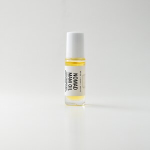 Puede incluir: Una botella de vidrio transparente de Nomad Mani Oil con tapa blanca. La botella contiene un l&iacute;quido amarillo y tiene una etiqueta con texto negro. El producto est&aacute; dise&ntilde;ado para el tratamiento de cut&iacute;culas con manteca de marula y aceite de jojoba.