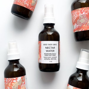 May include: Five amber glass bottles of Nectar Water face toner with white spray tops. Each bottle has a label with the text "BEIGE / DUSK / GREYS NECTAR WATER NOURISHING ROSE & HONEY FACE TONER" and a floral design. The bottles are 3 oz.