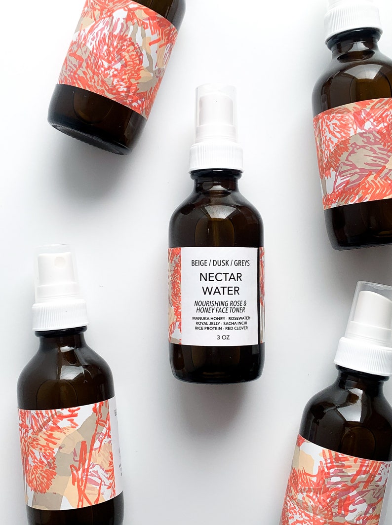 May include: Five amber glass bottles of Nectar Water face toner with white spray tops. Each bottle has a label with the text "BEIGE / DUSK / GREYS NECTAR WATER NOURISHING ROSE & HONEY FACE TONER" and a floral design. The bottles are 3 oz.