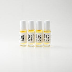 Puede incluir: Cuatro peque&ntilde;os frascos roll-on de vidrio transparente con tapas blancas est&aacute;n alineados. Cada frasco contiene un l&iacute;quido amarillo y tiene una etiqueta que dice "NOMAD MANI OIL". Las etiquetas tambi&eacute;n incluyen texto sobre el tratamiento de cut&iacute;culas.