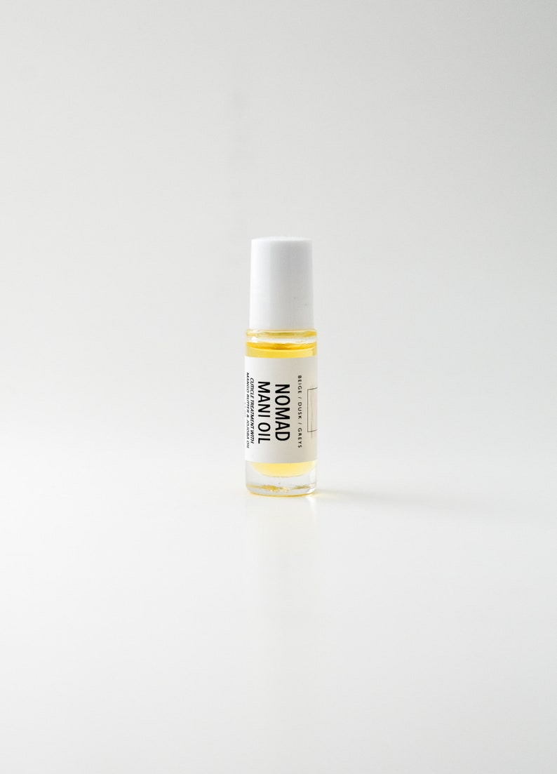 Puede incluir: Una botella de vidrio transparente de Nomad Mani Oil con tapa blanca. La botella contiene un l&iacute;quido amarillo y tiene una etiqueta con el nombre del producto y otro texto. El producto es un tratamiento para cut&iacute;culas.