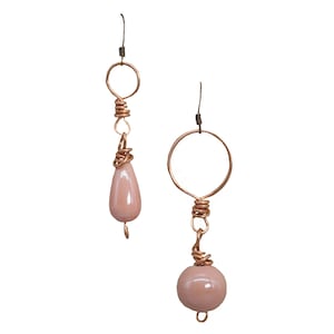 Puede incluir: Un par de pendientes hechos a mano con cuentas de vidrio rosa y alambre de cobre. Los pendientes están hechos con una cuenta en forma de lágrima en un lado y una cuenta redonda en el otro.