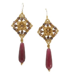 Op de afbeelding: Een paar goudkleurige oorbellen met een geometrisch ontwerp. Elke oorbel heeft een vierkante bovenkant met een bloemencentrum en bruine accenten, verbonden met een lange, druppelvormige, bordeauxrode steen. De oorbellen hebben een haaksluiting.