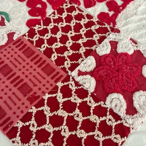 May include: Close-up of a patchwork textile featuring various red and white embroidered patterns. The designs include floral, geometric, and lattice motifs, creating a textured and visually rich composition. The fabric appears to be cotton or a similar material.